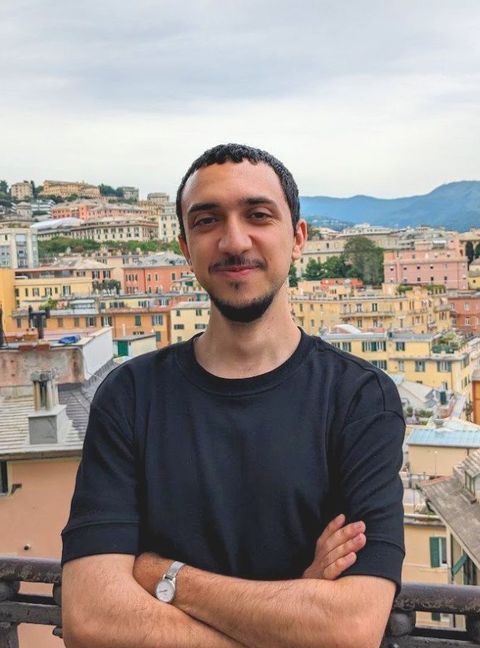 Mohammad Aldehayat, arms crossed, on a balcony above a hillside city.